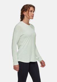 Jasnozielona, długosleeve'owa koszulka sportowa z okrągłym dekoltem, miękką teksturą i luźniejszym krojem. Posiada małe logo na klatce piersiowej oraz stębnowane wykończenie.