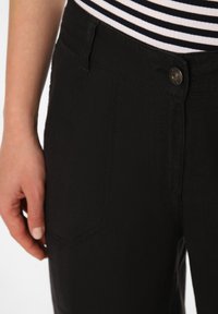 Black pants made of textured fabric with a visible front pocket and a metal button closure. Striped top shown partially at the top.