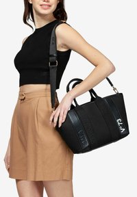 Borsa a tracolla nera con testo in rilievo e accenti lucidi, manici doppi e tracolla regolabile; design strutturato, materiale in tessuto.