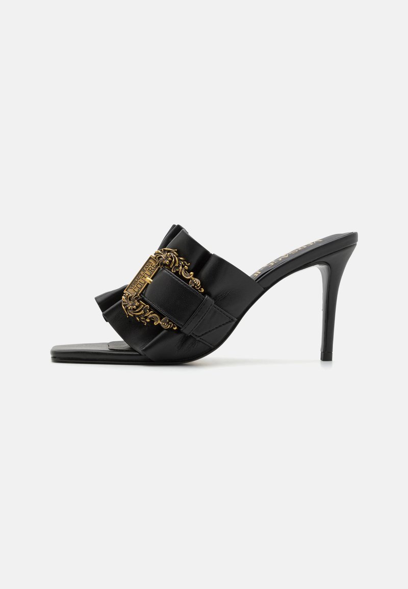 Sandálias de salto alto pretas com acabamento em cetim, apresentando uma fivela decorativa dourada ousada e um design de tiras acolchoadas.