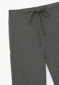 Mørkegrå bukser lavet af tekstureret stof, med elastisk talje og snøring samt en sideslids for ekstra stil.