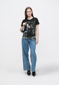 Black t-shirt with a graphic design featuring a cat, paired with light blue wide-leg jeans and black heeled boots.
