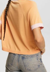 Orange cropped t-shirt med pink ribbede ærmer, stylet med falmede blå jeans. Blød tekstur og enkelt design med en afrundet kant.