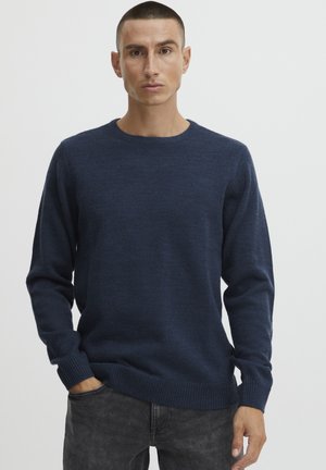 Navy blue knitted sweater with crew neckline, ribbed cuffs, and hem, textured fabric, worn with gray jeans.
