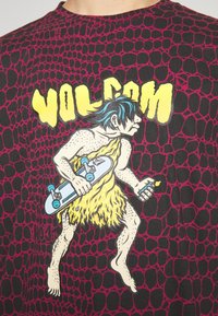 Grafisk T-shirt med en tegneseriefigur med blåt hår, der holder et skateboard. Baggrunden har et mønster i sort og lilla. "VOLCOM" tekst i gul.