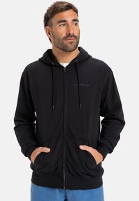 Sweatshirt preto com fecho zip, com capuz ajustável por cordão, bolsos frontais e detalhe de logotipo discreto. Tecido suave com um corte descontraído.