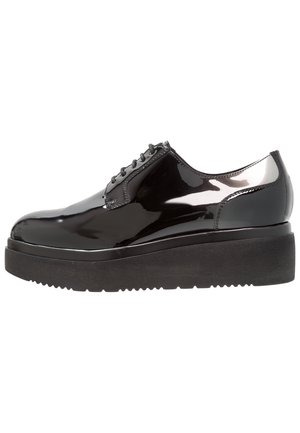 Chaussure plateforme en cuir verni noir avec semelle épaisse noire et lacets noirs, talon bas et finition lisse et brillante.