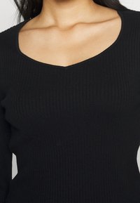 Svart ribbat stickat topp med djup V-ringning, långa ärmar och figurnära passform. Mjuk textur och subtil stretch för komfort.