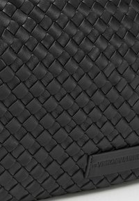 Borsa in pelle intrecciata nera con una superficie testurizzata e un'etichetta di marca rettangolare. Presenta un design intrecciato intricato e una finitura liscia.