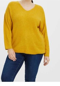 Maglione a coste giallo senape con scollo a V e spalle cadute, caratterizzato da una vestibilità rilassata e orlo grezzo. Abbinato a jeans blu scuro.