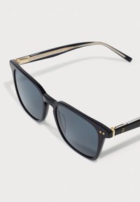 Occhiali da sole rettangolari neri con lenti grigie. Presentano accenti dorati sulle tempie e una montatura nera texturizzata. Design pulito e moderno.