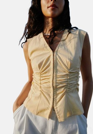 Top sans manches jaune au design ajusté, avec ruching à l'avant et décolleté en V, fabriqué en tissu léger.
