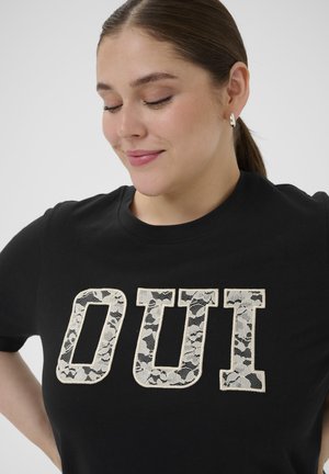 Sort T-shirt med store, hvide bogstaver med blonder, der staver "OUi." Rund halsudskæring og korte ærmer med en blød bomuldstekstur.