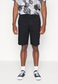 Black shorts made of lightweight fabric, featuring a simple design with a smooth texture and knee-length cut, paired with black sneakers and white socks.