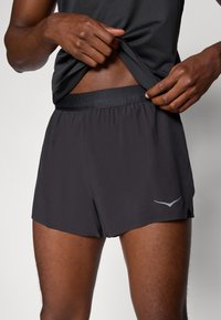 Svarte idrettsshorts laget av lettvektstoff, med elastisk midje og en liten logo på nedre del.