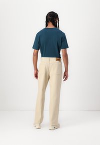 Men's teal cotton t-shirt and beige straight-leg pants with a brown leather label, featuring two back pockets and a relaxed fit.