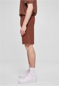 Bruine katoenen shorts met een elastische tailleband en zijzakken, gecombineerd met witte sneakers en geribbelde witte sokken, gezien vanaf de zijkant.