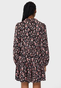 Zwarte bloemenjurk met lange mouwen, smocktail en een uitlopende rok. Bevat roze en witte bloemen op een donkere achtergrond.