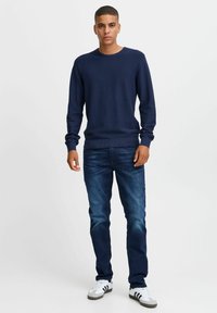 Marinefarget teksturert genser, langermet, rund hals, kombinert med falmet blå jeans og hvite joggesko med svarte detaljer.