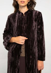 Manteau long en velours de couleur violet foncé avec une texture rayée. Doté d'un col mandarin et de boutons recouverts de tissu floral.