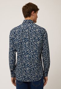 Langdurige mouwblouse van donkerblauwe stof met een wit bloemen- en wijnpatroon. Heeft een kraag en een rugplooitje voor een relaxte pasvorm.