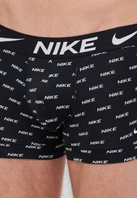 Schwarze Boxershorts mit durchgehendem weißen Nike-Logo-Print, ausgestattet mit einem elastischen Bund mit Nike-Branding und einem figurnahen Design.