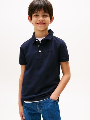 Navy blue polo shirt with a collar, featuring two buttons and a small logo. Paired with blue denim jeans, showing a relaxed fit.
