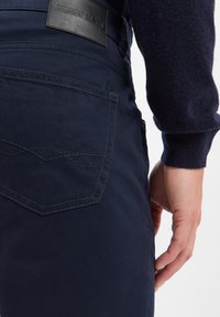 Granatowe dżinsy z bawełny z skórzaną metką oznaczoną "ANDREW JAMES", z dopasowanym ściegiem na tylnej kieszeni oraz fasonem slim fit.