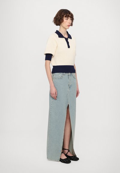 Haut tricoté crème avec col et poignets marine ; jupe maxi en denim bleu clair taille haute avec une fente avant ; ballerines noires à pois.