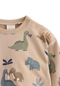 Beige Langarmhemd mit Dinosaurier-Mustern in Grün, Blau und Braun. Verfügt über Druckknopfverschlüsse an den Schultern und einen gerippten Ausschnitt.
