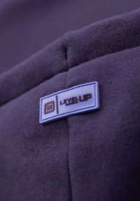 Tissu violet avec une texture lisse présentant une étiquette rectangulaire. L'étiquette est blanche avec un contour bleu et du texte marron : "NIVEAU SUPÉRIEUR".