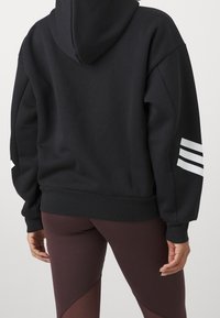 Czarna bluza z dużym kapturem i trzema białymi paskami na prawym rękawie. Obcisłe bordowe legginsy o geometrycznym kroju.