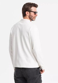 Weißes langärmliges Shirt mit lockerer Passform, ausgestattet mit Rundhalsausschnitt und weichem Material, kombiniert mit schwarzen, zerrissenen Jeans.