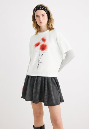 Fiatal nő fehér, piros pipacs mintás ingben, alatta szürke hosszú ujjú, fekete tűselyem szoknyával, fekete fejpánt ezüst szegecsekkel.