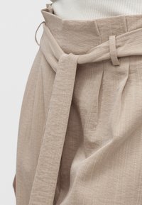 Pantalones beige de cintura alta con un cinturón de tela atado en un nudo, combinados con una camiseta de canalé clara metida dentro.