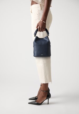 Navy leather handbag with a structured shape, short handle, and visible stitching details. Paired with light-colored, frayed pants and black heels.