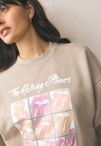 Beżowa bluza z prążkowanym dekoltem z kolorowym logo Rolling Stones w układzie w kratkę; miękka w dotyku i luźnego kroju.