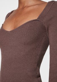 Brun, randig långärmad topp med fyrkantig halsringning och figurnära silhuett. Har vertikal textur och sömdetaljer längs kroppen.
