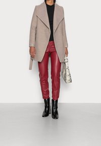 Ljusbeige kappa med bred krage, svart topp, röda läderbyxor och svarta ankelstövlar. Accessoarer med en vit handväska i ormskinn.