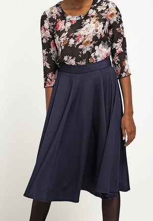 Haut transparent noir à motif floral avec des manches trois-quarts, assorti à une jupe A-line bleu marine unie, mettant en avant un tissu lisse et fluide.