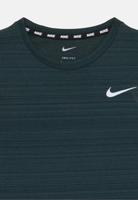 Mørkegrønn Nike Dri-FIT treningsskjorte med hvit Nike swoosh-logo på brystet og gjentatt Nike-tekst på den indre kragen.