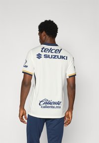 Bijela kratkosbijela majica s plavim i zlatnim detaljima. Ima logotipe sponzora: "telcel", "Suzuki" i "Caliente" na leđima. Tkanina teksturirana.