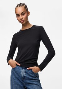 Sort langærmet top med rund hals, båret sammen med højtaljede lyseblå denim jeans. Glat tekstur, tætsiddende silhuet.