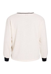 Baltā teksturētā auduma ar melnām aprocēm garā piedurkņu augšdaļa. Brīvs siluets, apaļš kakla izgriezums ar kontrastējošu apdari un bez aizdares detaļām.