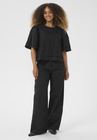 Svart tvådelad outfit med en texturerad topp med puffärmar och broderade detaljer, kombinerad med vida byxor och prydda skor.