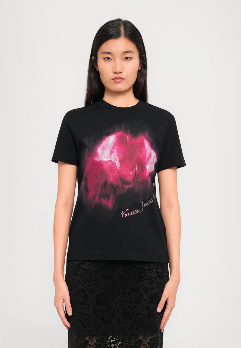 Black cotton t-shirt featuring a pink graphic design on the front, with text at the bottom. Model wears a black lace skirt.