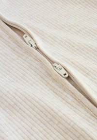 Close-up van twee beige ritsen op geribd, licht roomkleurig stof, waarvan één half open en de andere helemaal dicht.