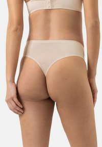 Beige saumaton thong valmistettu sileästä, venyvästä materiaalista. Siinä on matalavyötärö ja minimaalinen peitto takana.