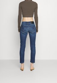 Vaqueros de mezclilla azul oscuro con corte ajustado, combinados con una blusa corta de manga larga marrón. Presenta dos bolsillos traseros y costuras mínimas.