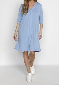 Světle modré šaty ke kolenům s výstřihem ve tvaru V, tříčtvrtečními rukávy a bočními kapsami, vyrobené z měkké, hladké tkaniny.